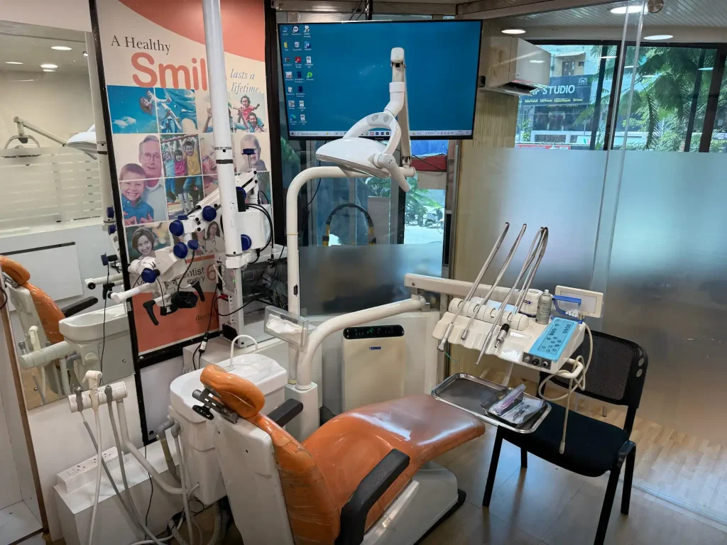 Mobile dental equipment unit with suction hoses and instrument tray in a modern clinic room.